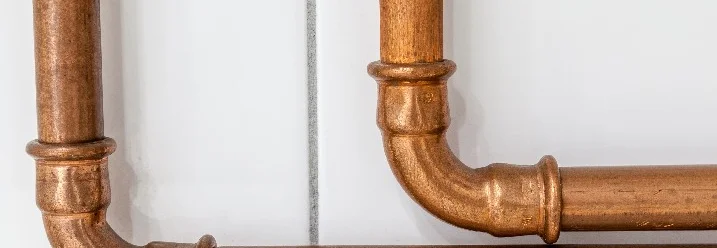 Zwei kupferne Rohre an weißer Wand.